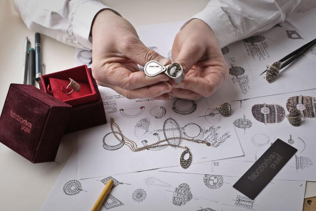 Hands holding a piece of jewelry over jewelry design sketches