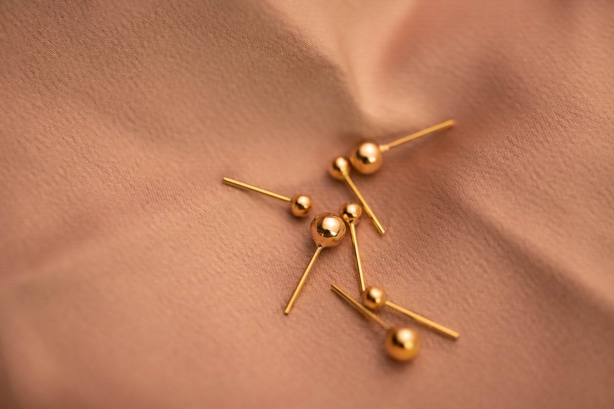 Small gold ball stud earrings on a brown fabric surface