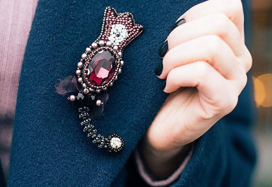 Hand touching a decorative brooch pinned to a teal jacket