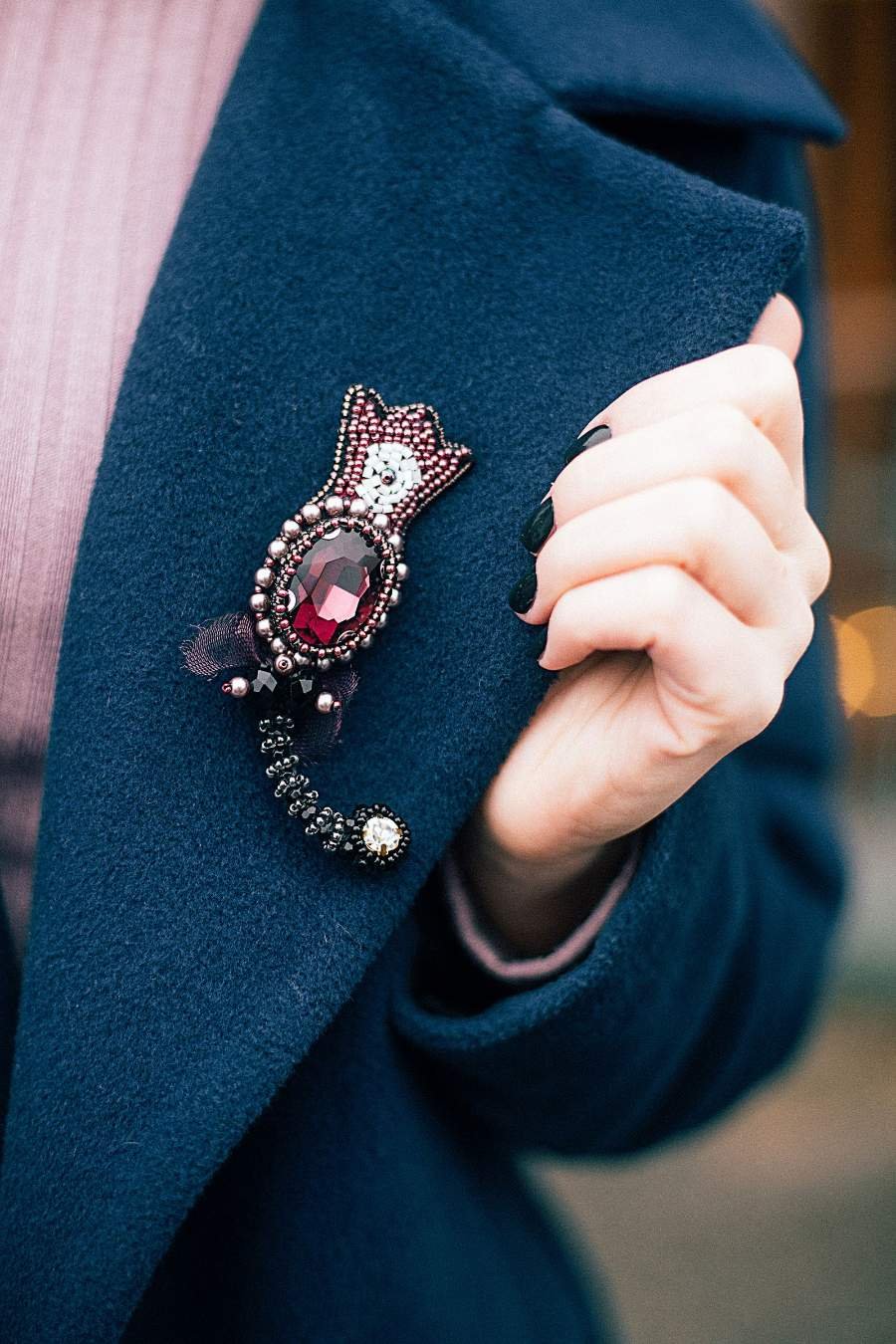 Hand touching a decorative brooch pinned to a teal jacket