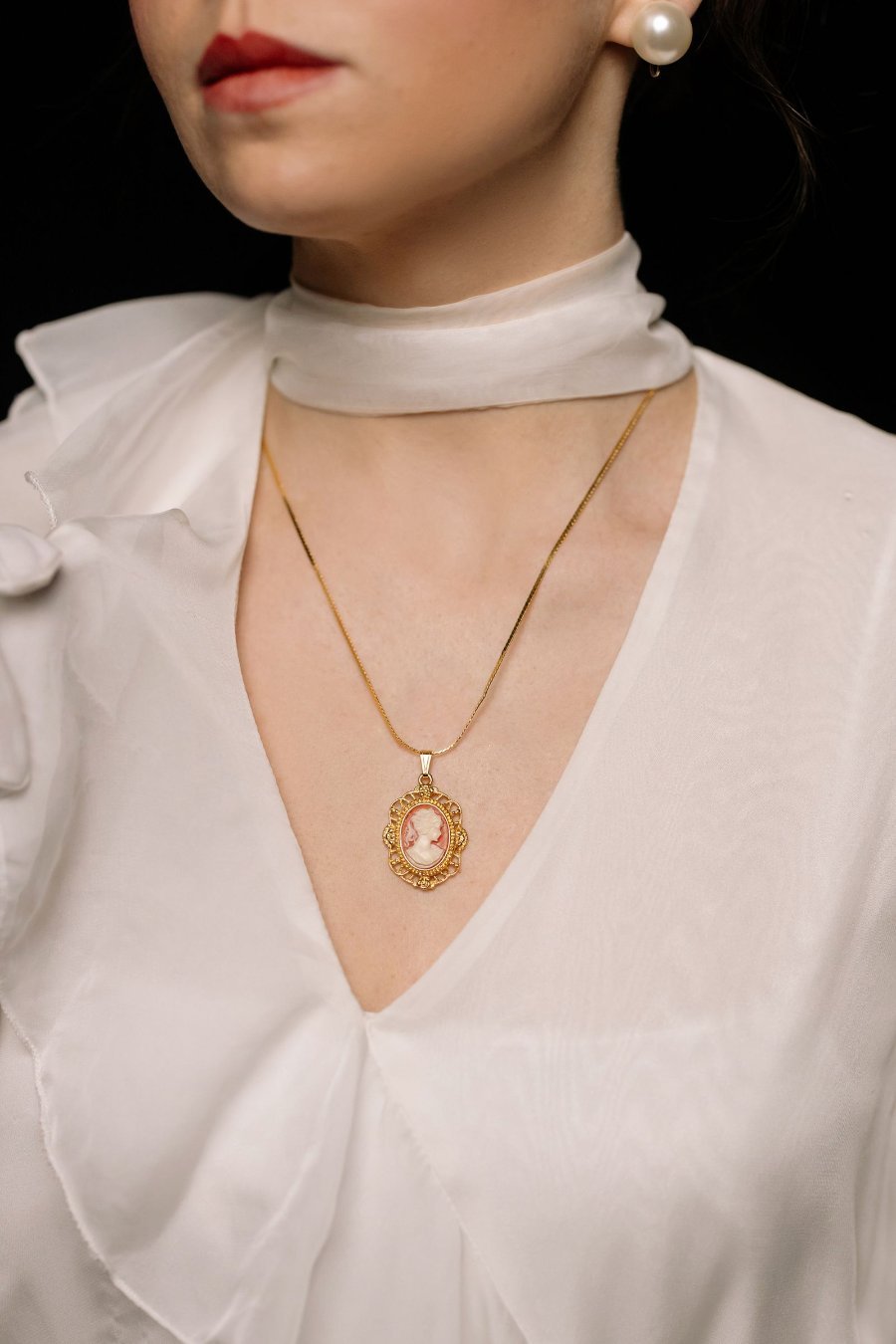 Oval pendant on a gold chain worn with a white blouse